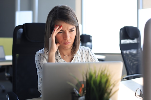 Donna d'affari frustrata che sembra esausta mentre è seduta al suo posto di lavoro.