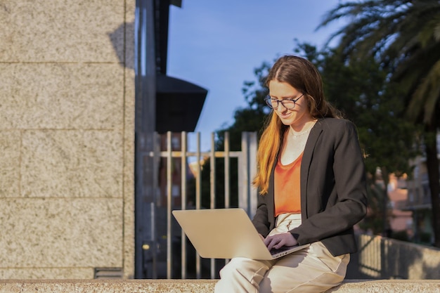 Donna d'affari in abiti casual che utilizza un computer portatile seduto all'esterno di un edificio