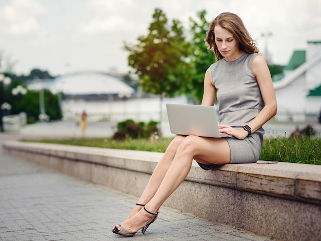 Donna d'affari in abito elegante utilizzando laptop sulla strada