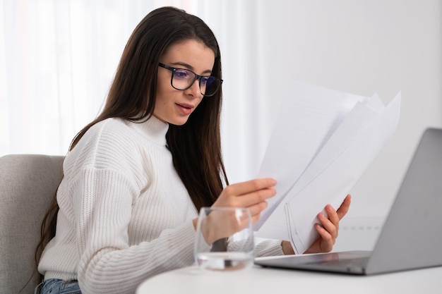 Donna d'affari in camicia bianca utilizzando il computer portatile e controllando i documenti