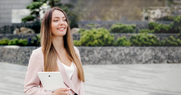 Donna d'affari in giacca e cravatta sorridente tenendo un tablet e distogliendo lo sguardo