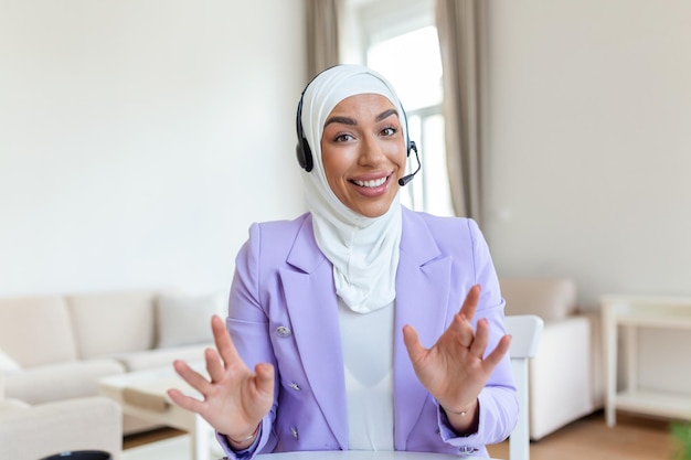 Donna d'affari in hijab con una chat video sul laptop Donna seduta al bar e fare videochiamate utilizzando auricolari e computer portatile