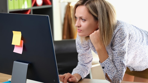 Donna d'affari in piedi alla sua scrivania e guarda il manager femminile del monitor del computer