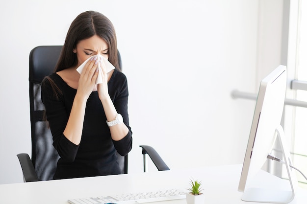 Donna d'affari malata che soffre al lavoro dietro la scrivania nel suo ufficio e ha problemi di allergia