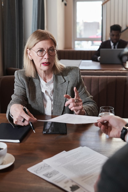 Donna d'affari matura che consulta l'uomo sui documenti durante la riunione al caffè