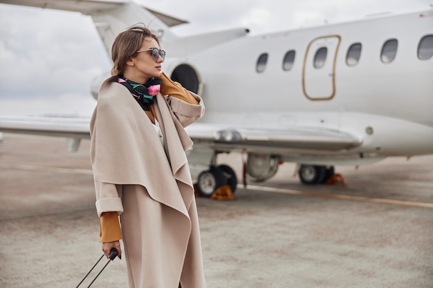 Donna d'affari matura in cappotto vicino al suo jet in aeroporto