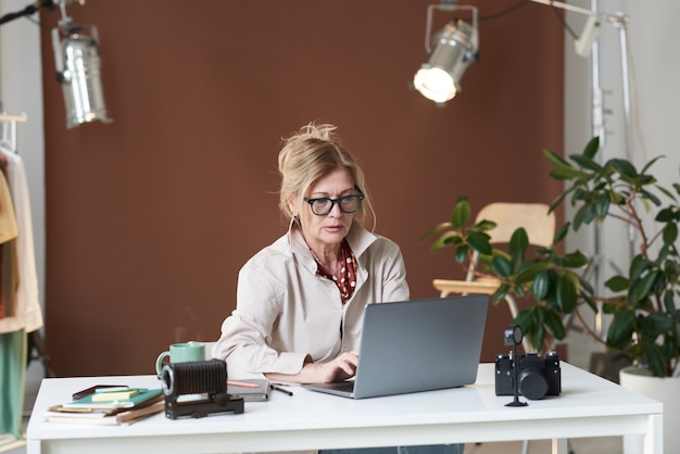 Donna d'affari matura seduta al tavolo e digitando sul computer portatile che lavora online in ufficio