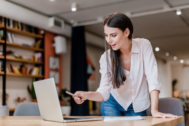 Donna d'affari millenaria nel suo ufficio che controlla le informazioni dal suo computer portatile