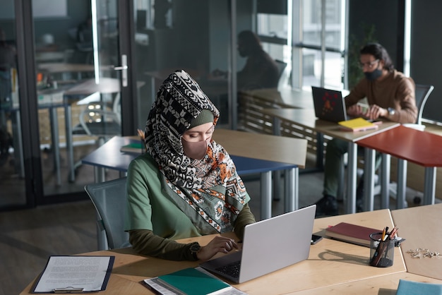 Donna d'affari musulmana che digita sul laptop e lavora online sul posto di lavoro in ufficio