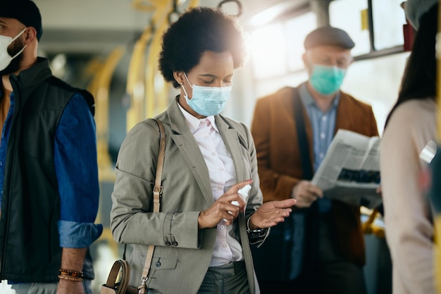 Donna d'affari nera che si disinfetta le mani mentre si sposta con i mezzi pubblici