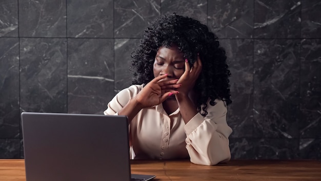 Donna d'affari nera con tipi di capelli ricci pigramente sul laptop