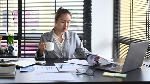 Donna d'affari professionale che beve caffè e lavora in un ufficio moderno