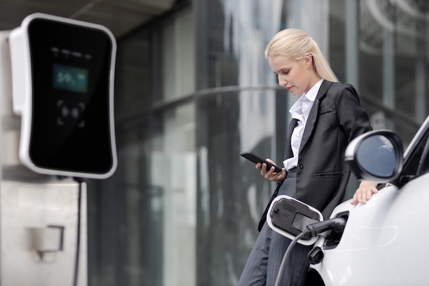 Donna d'affari progressista con smartphone mockup con EV alla stazione di ricarica