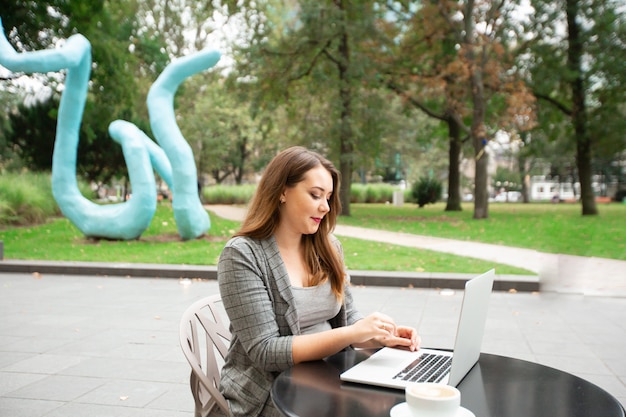 Donna d'affari seduto in una caffetteria sulla strada della città, lavorando a un computer portatile.