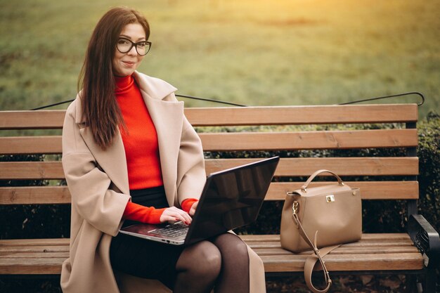 Donna d&#39;affari seduto su una panchina e lavorando su un computer portatile