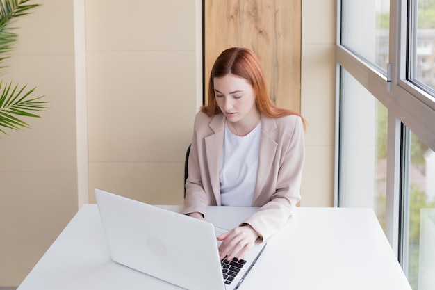 Donna d'affari seria che lavora al computer portatile seduta alla scrivania dell'ufficio