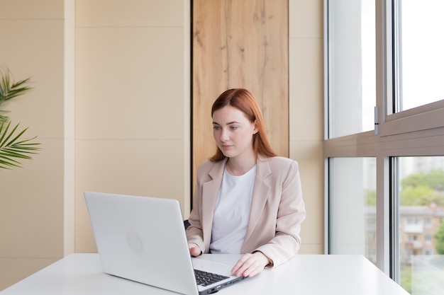 Donna d'affari seria che lavora al computer portatile seduta alla scrivania dell'ufficio