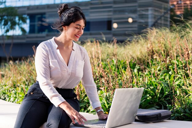 Donna d'affari sorridente che lavora con il suo computer portatile seduto in un parco nel distretto finanziario, concetto di imprenditore digitale e stile di vita urbano, copia spazio per il testo