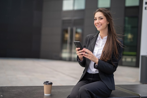 Donna d'affari sorridente che usa il suo smartphone mentre è seduto su una panchina