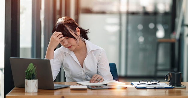 Donna d'affari stressata che lavora in ufficio sul laptop che sembra preoccupata, stanca e sopraffatta