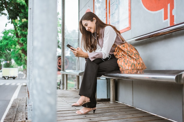 Donna d'affari su una stazione degli autobus in attesa che arrivi l'autobus mentre si usa il telefono