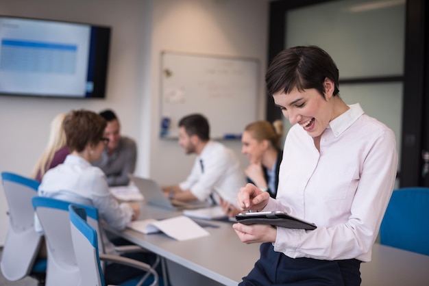 donna d'affari sull'incontro con il tablet computer, blured gruppo di persone sullo sfondo all'interno dell'ufficio di avvio moderno e luminoso