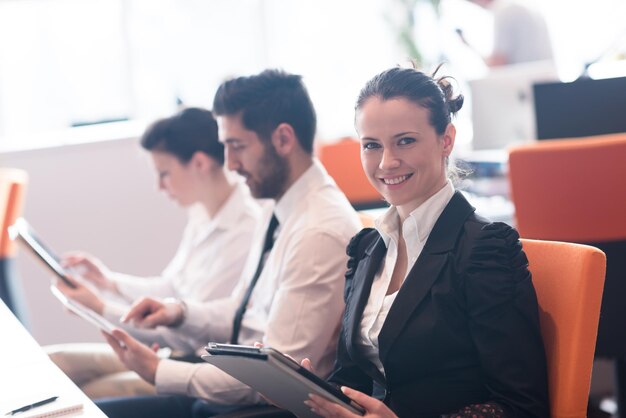 donna d'affari sull'incontro con il tablet computer, blured gruppo di persone sullo sfondo all'interno dell'ufficio di avvio moderno e luminoso