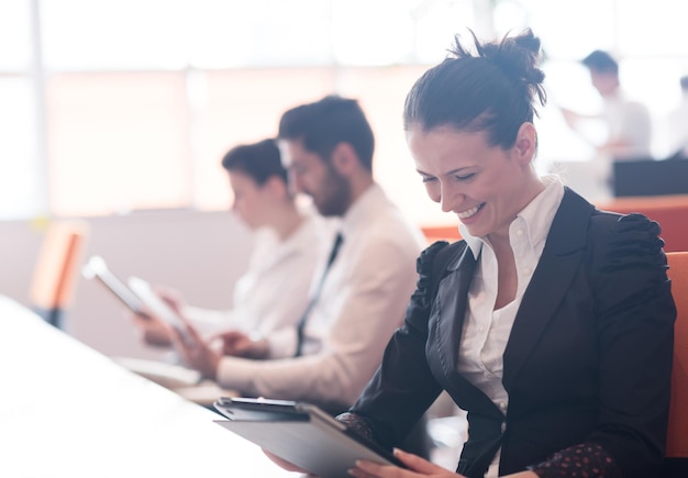 donna d'affari sull'incontro con il tablet computer, blured gruppo di persone sullo sfondo all'interno dell'ufficio di avvio moderno e luminoso