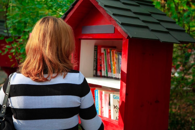 Donna dai capelli bionda che guarda i libri nella biblioteca. libreria in legno di colore rosso. biblioteca nel for