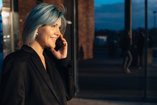 Donna dai capelli blu parla al telefono mentre posa fuori davanti al sole
