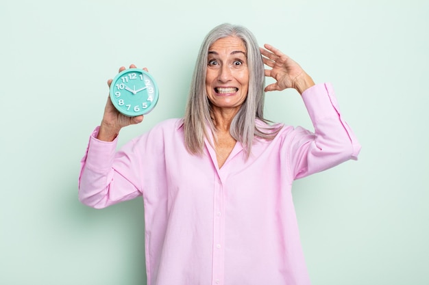 Donna dai capelli grigi di mezza età che si sente stressata, ansiosa o spaventata, con le mani sulla testa. concetto di sveglia