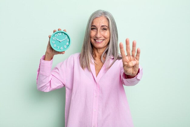 Donna dai capelli grigi di mezza età che sorride e sembra amichevole, mostrando il numero quattro. concetto di sveglia