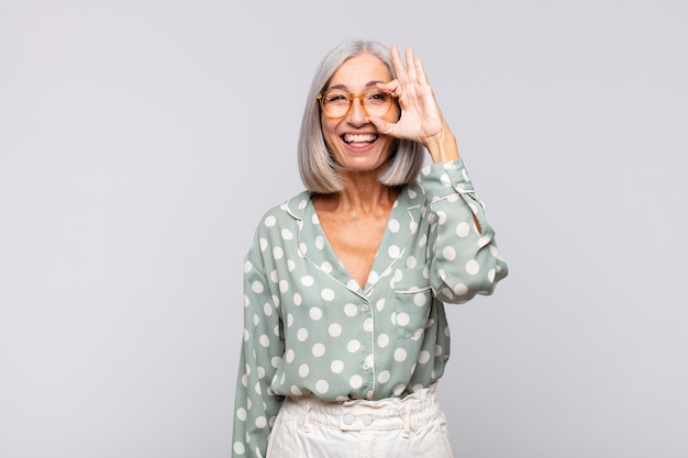 Donna dai capelli grigi sorridente felicemente con faccia buffa, scherzando e guardando attraverso lo spioncino