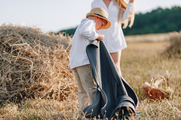 Donna dai capelli lunghi abbastanza bionda con figlio piccolo biondo al tramonto rilassante nel campo e assaporando la frutta da un cestino di paglia. estate, agricoltura, natura e aria fresca in campagna.