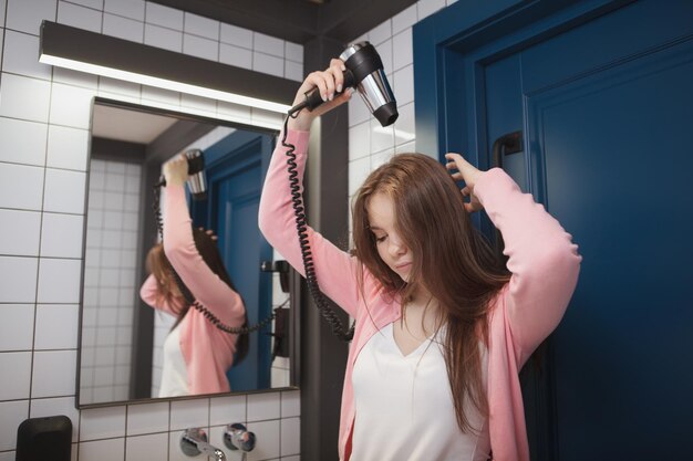 Donna dai capelli lunghi che usa l'asciugacapelli nel bagno della camera d'albergo