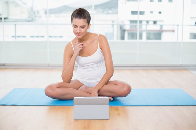 Donna dai capelli marrone naturale concentrata in abiti sportivi bianchi che esaminano un pc della compressa