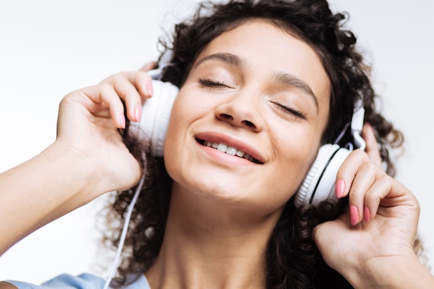 donna dai capelli ricci che ascolta la musica in cuffie bianche e se le preme contro le orecchie chiudendo gli occhi per la gioia