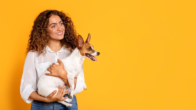 Donna dai capelli ricci che tiene amorevolmente un Jack Russell Terrier su sfondo giallo