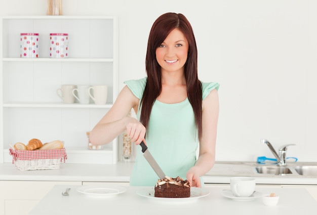 Donna dai capelli rossi attraente che taglia una certa torta nella cucina