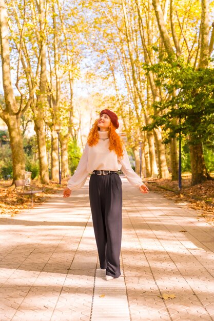 Donna dai capelli rossi che cammina attraverso un parco forestale cittadino sorridendo al tramonto