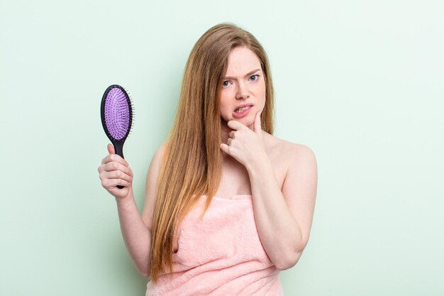 donna dai capelli rossi con la bocca e gli occhi spalancati e la mano sul mento. concetto di pettine per capelli