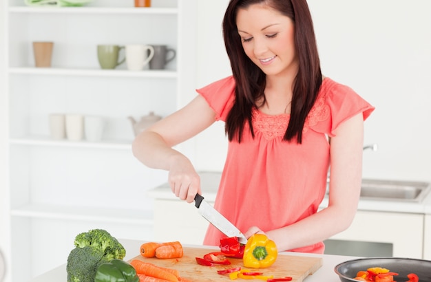 Donna dai capelli rossi splendida che taglia alcune carote nella cucina