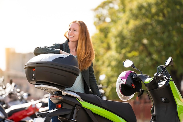 Donna dai capelli rossi sulla sua moto in un parcheggio che parla su smartphone