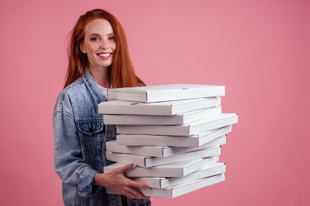 Donna dai capelli rossi zenzero abbastanza lunga che tiene molte scatole con snack fast food isolato sfondo rosa studio di consegna per il concetto di festa a casa