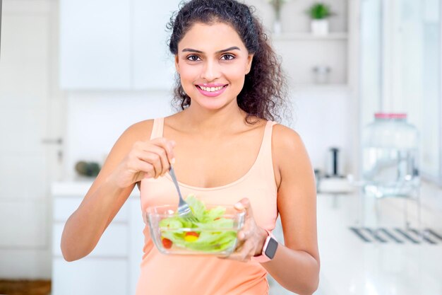 Donna dei capelli ricci che mangia una ciotola di gustosa insalata