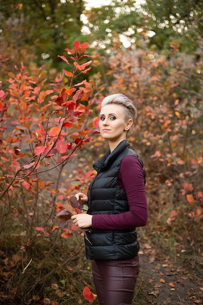 Donna dei pantaloni a vita bassa nella priorità bassa della foresta di autunno con gli alberi dorati e rossi