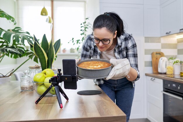 Donna del blog alimentare che cucina la torta di mele a casa registrando la ricetta sullo smartphone