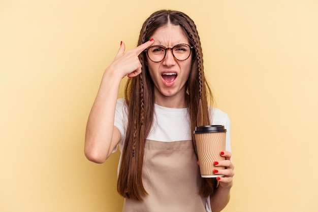 Donna del cameriere del ristorante che tiene un caffè da asporto isolato su sfondo giallo che mostra un gesto di delusione con l'indice.