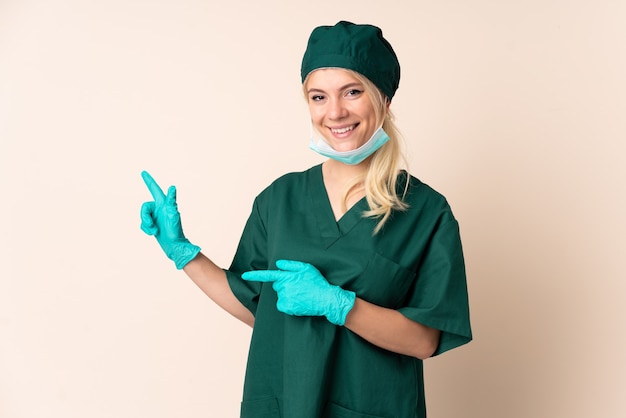 Donna del chirurgo in uniforme verde sopra il dito puntato della parete isolata al lato