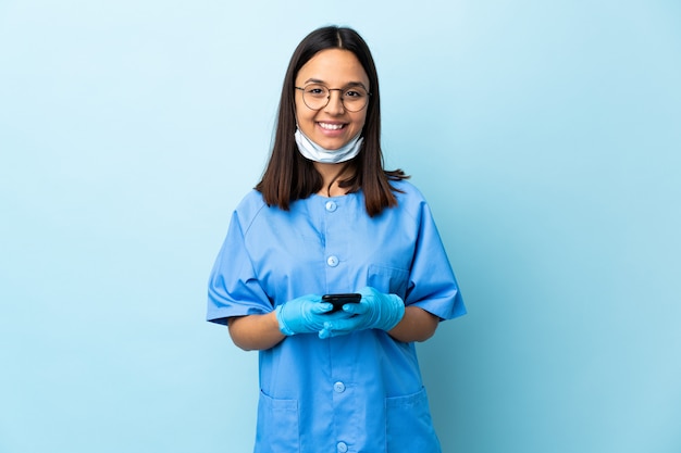 Donna del chirurgo sopra la parete blu che invia un messaggio con il cellulare